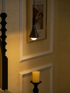 A black Clérachic pendant glows warm against a golden panelled wall, with a carved bedpost and a candle nearby.