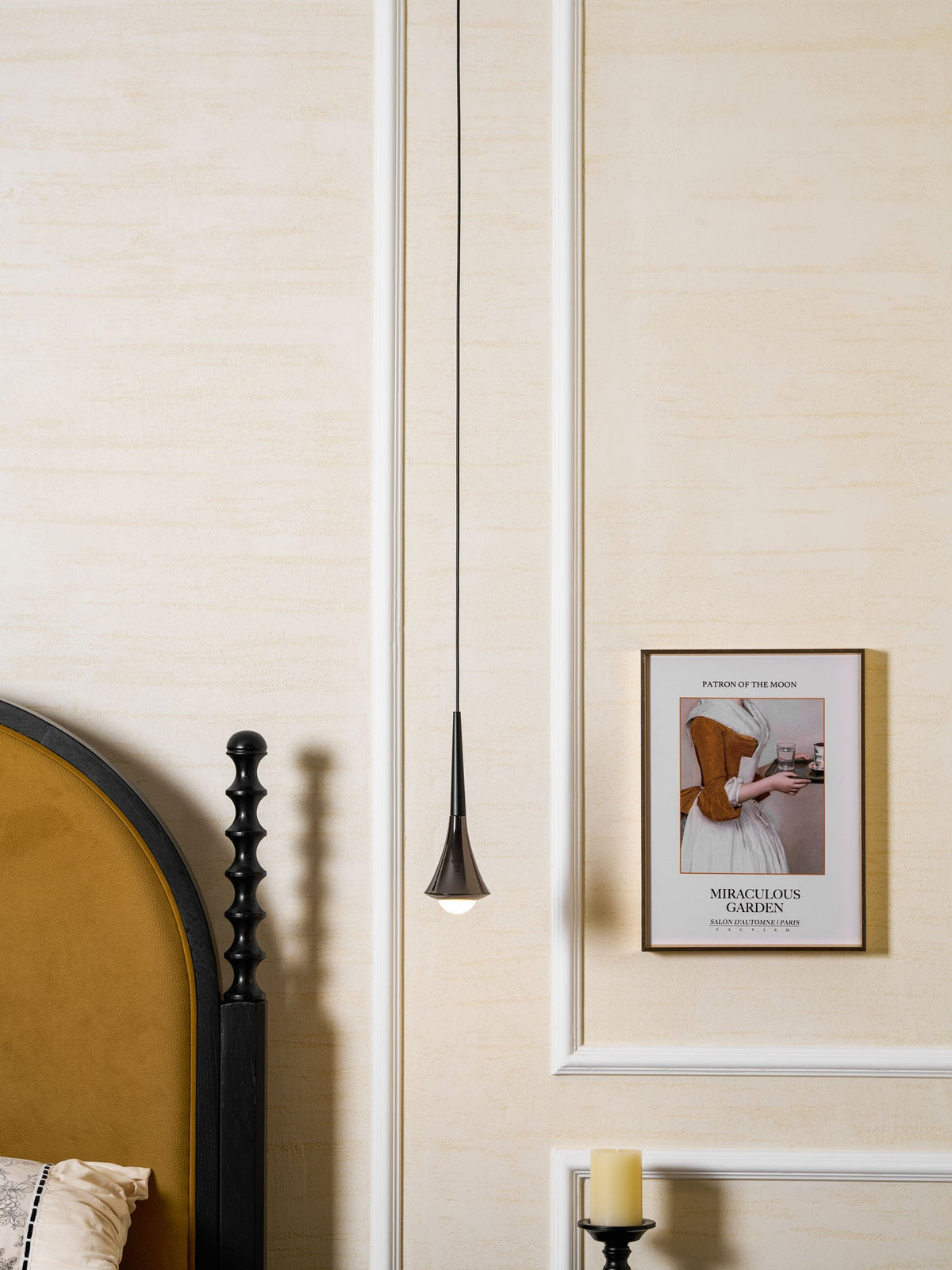 A slim Clérachic pendant hangs on a long cord beside a mustard headboard and a framed poster in a cream bedroom.