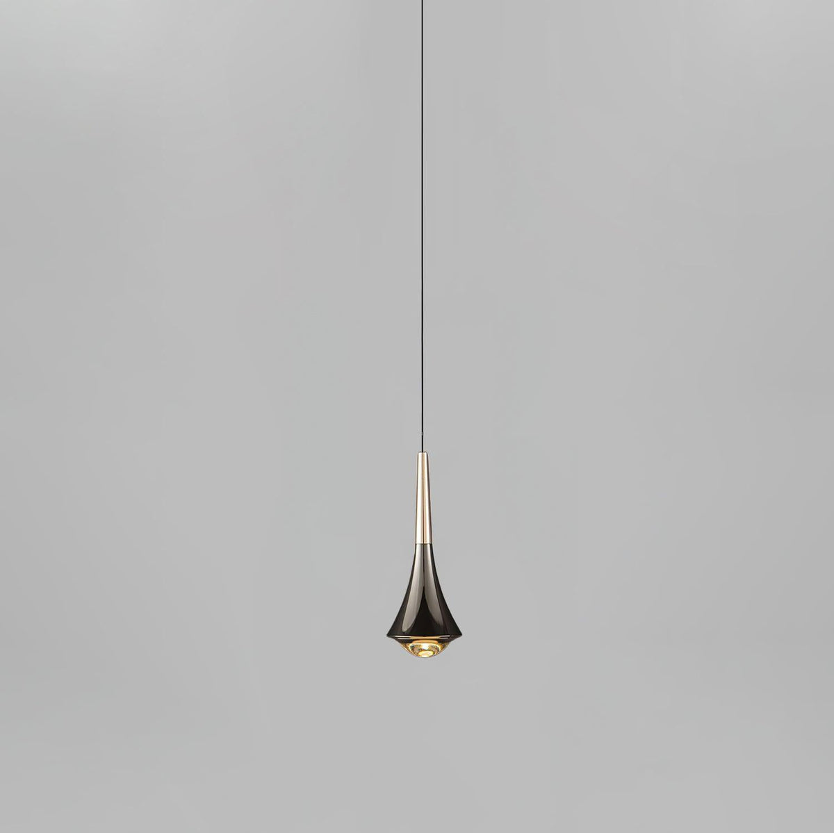 A Clérachic pendant with a flared dark chrome body and a pale champagne neck, on a thin cord against light grey.