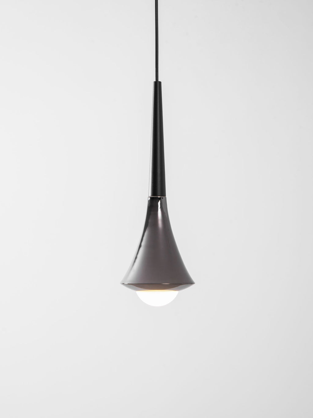A black-necked Clérachic pendant with a chrome flare, lit with a bright opal bulb at its base, on a pale backdrop.