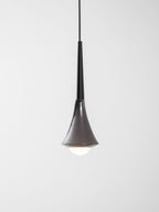 A black-necked Clérachic pendant with a chrome flare, lit with a bright opal bulb at its base, on a pale backdrop.