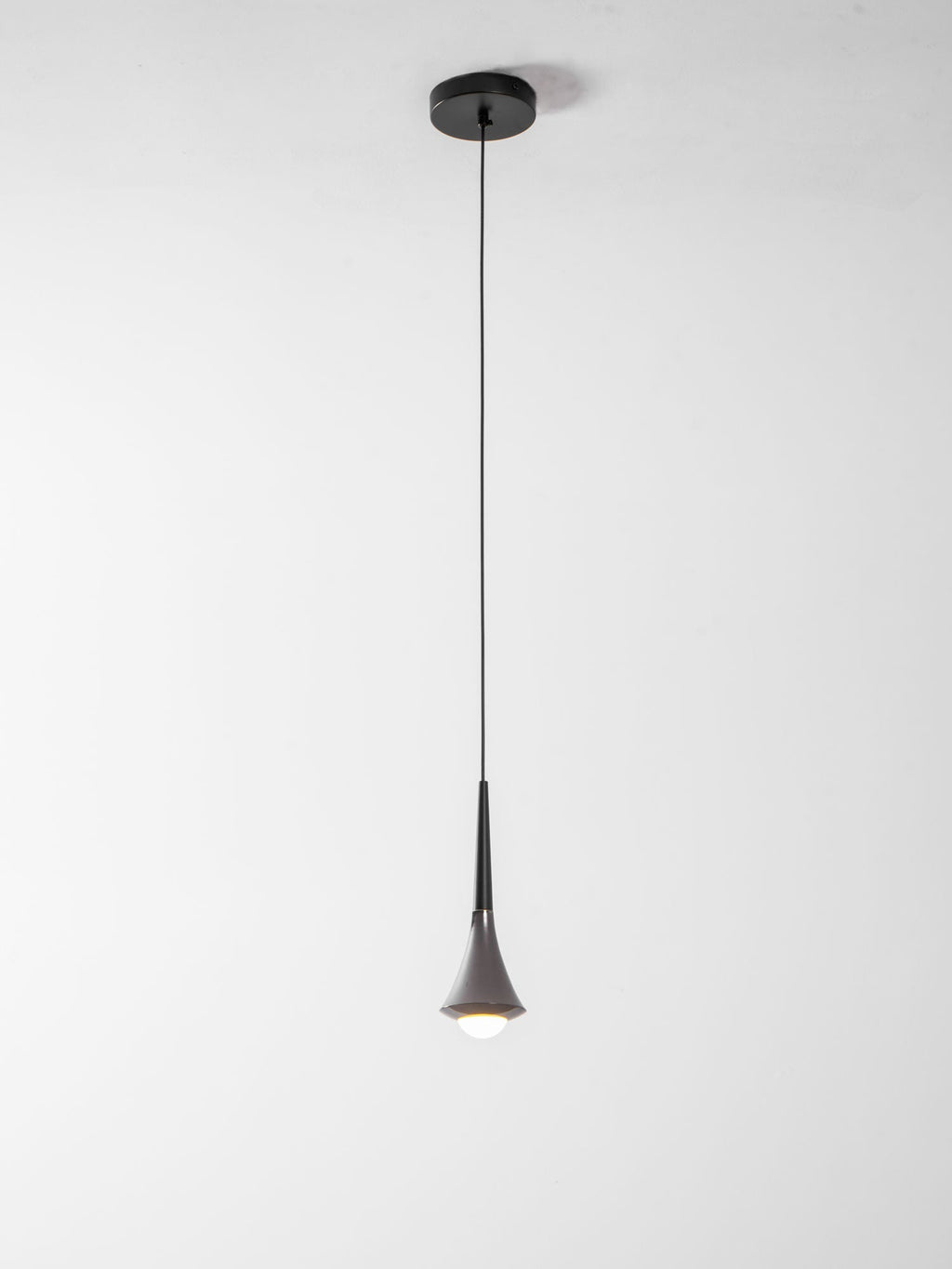 A Clérachic pendant on a long thin cord from a small black canopy, with a lit opal bulb at the tip, on a pale backdrop.