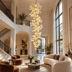 Clérachic cascading chandelier in an arched entrance hall with a wrought-iron balustrade, with terracotta armchairs and a round table below.