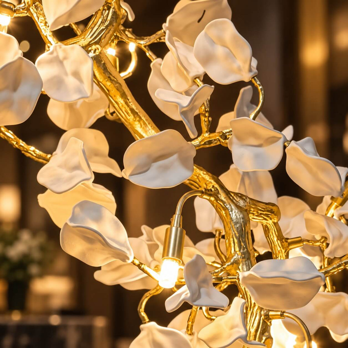 Close view of the white ceramic petals and the gold-toned branches holding the bulbs on this Clérachic cascading chandelier.