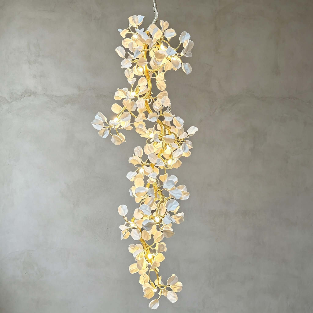 Lit Clérachic cascading chandelier of ceramic petals and gold-tone branches against a grey plaster wall.