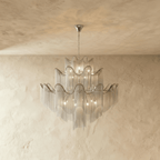 Clérachic silver tiered chandelier of fine chain fringe with wavy ribbon rims, hung from a chain against a pale limewashed wall.