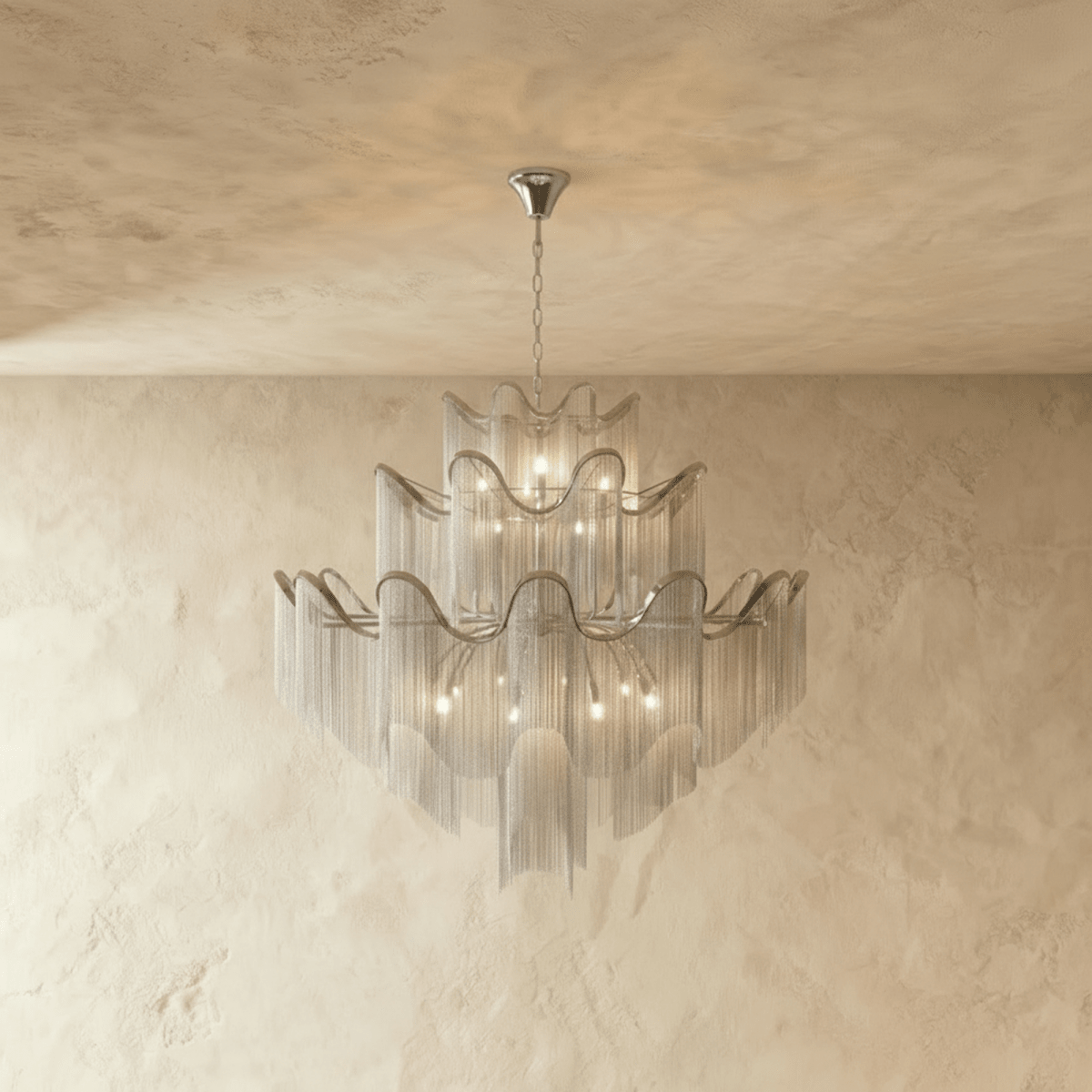 Clérachic silver tiered chandelier of fine chain fringe with wavy ribbon rims, hung from a chain against a pale limewashed wall.