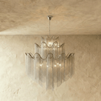 Clérachic silver three-tier chandelier with long chain fringe, shown lit and hung from a chain before a plaster wall.