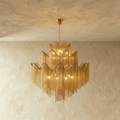 Clérachic gold tiered chain-fringe chandelier with warm bulbs glowing, hung on a fine chain against a limewashed wall.