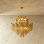 Clérachic gold tiered chain-fringe chandelier with warm bulbs glowing, hung on a fine chain against a limewashed wall.