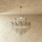 Clérachic silver tiered chain-fringe chandelier lit warmly, hanging from a slim chain in front of a limewashed wall.
