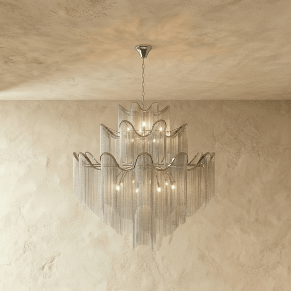 Clérachic silver tiered chain-fringe chandelier lit warmly, hanging from a slim chain in front of a limewashed wall.