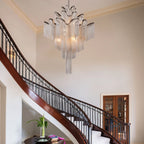 Clérachic silver chain-fringe chandelier hanging in a double-height stairwell beside a curved staircase with a wrought-iron rail.
