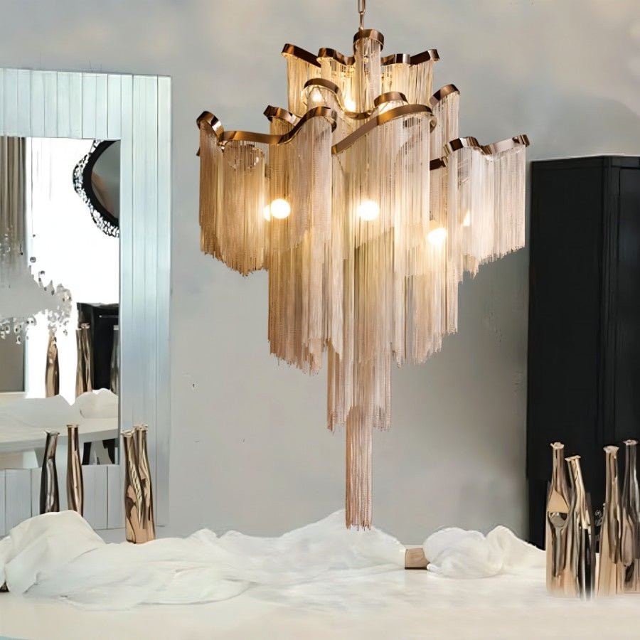Clérachic chain-fringe chandelier lit above a white table, with a tall mirror and gold vases in a modern interior.