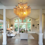 Clérachic gold chain-fringe chandelier hung in a bright open-plan living room with tall arched windows and wood floors.