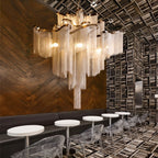 Clérachic silver chain-fringe chandelier lit above round white tables and clear chairs in a dark wood-panelled café.