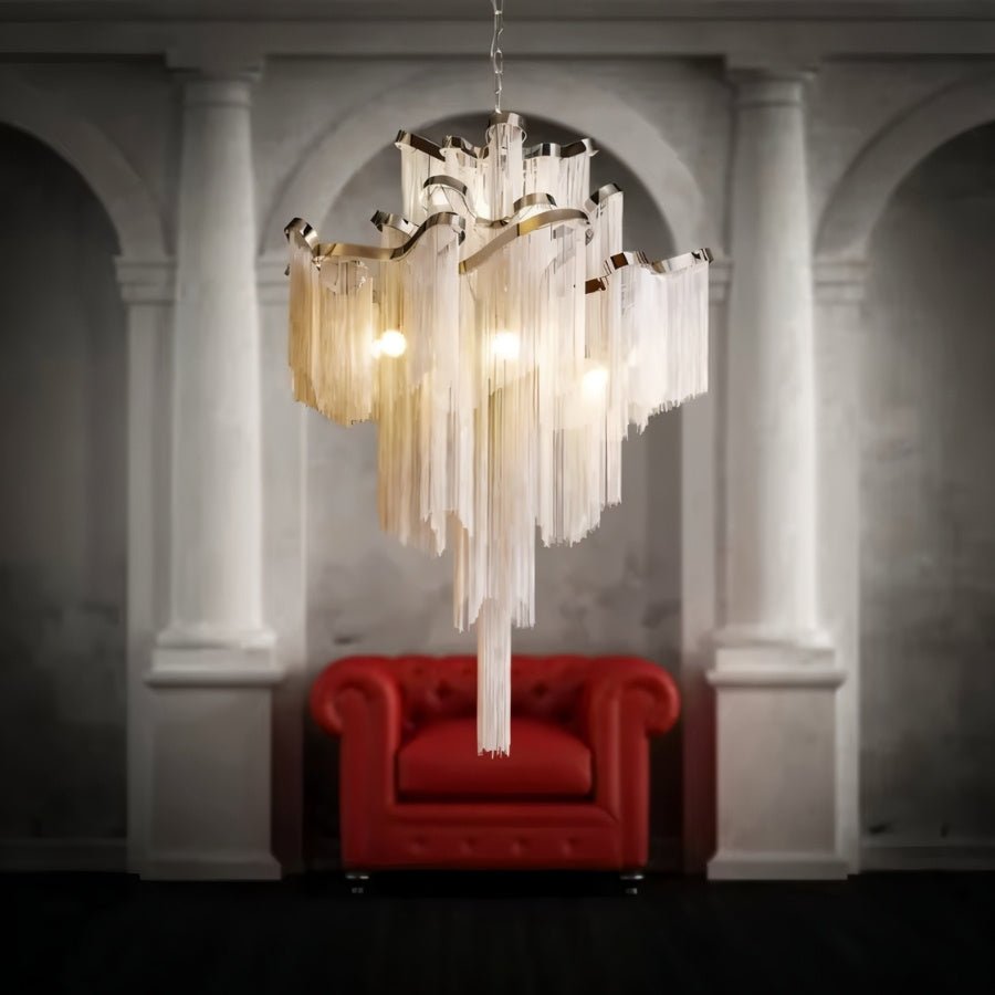 Clérachic chain-fringe chandelier lit above a red leather armchair in a room with pale classical columns and arches.