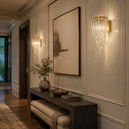 Warm light spills from this Clérachic wall light, with its looped glass strands and gold backplate, beside a large abstract canvas.