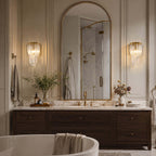 A pair of Clérachic wall lights flank an arched gold-framed mirror above a vanity, with a freestanding bath below.