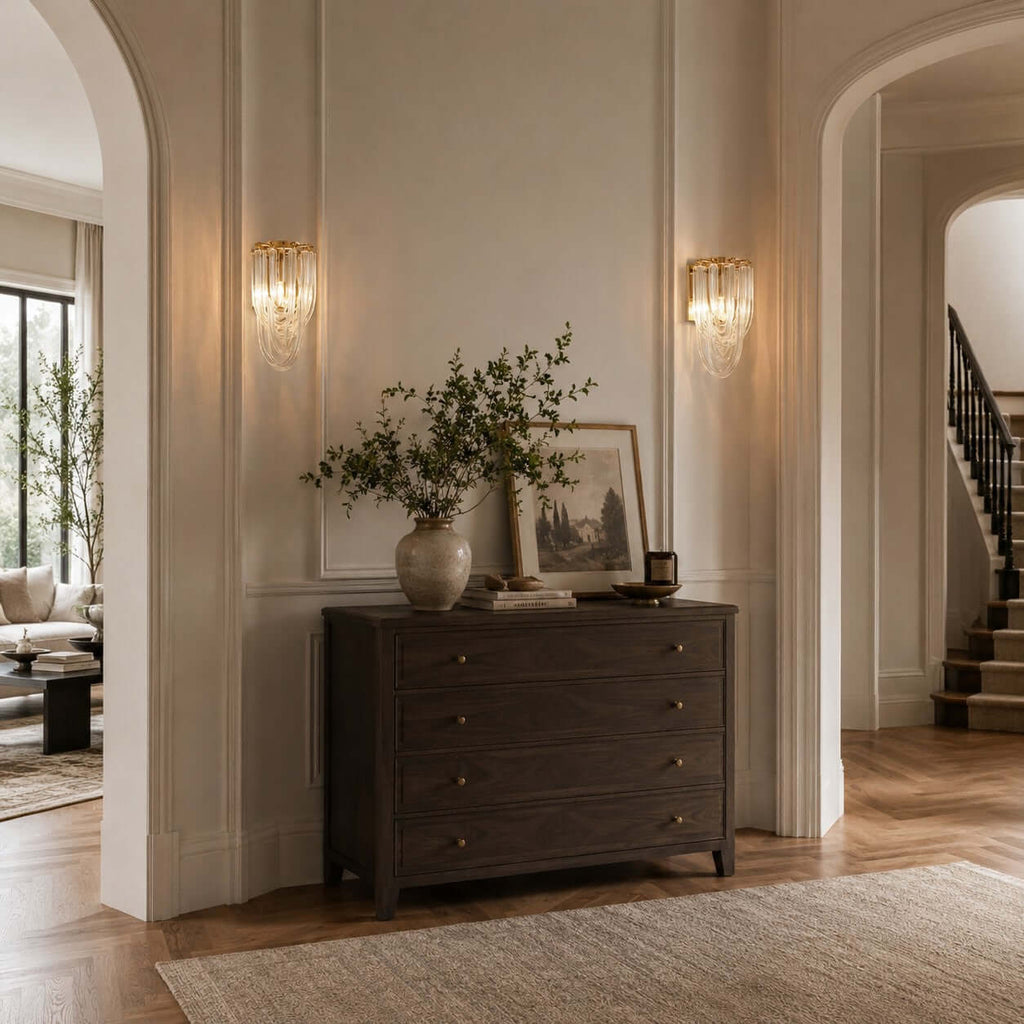 Two Clérachic wall lights light a panelled wall above a dark chest of drawers, beside a pair of arched doorways.