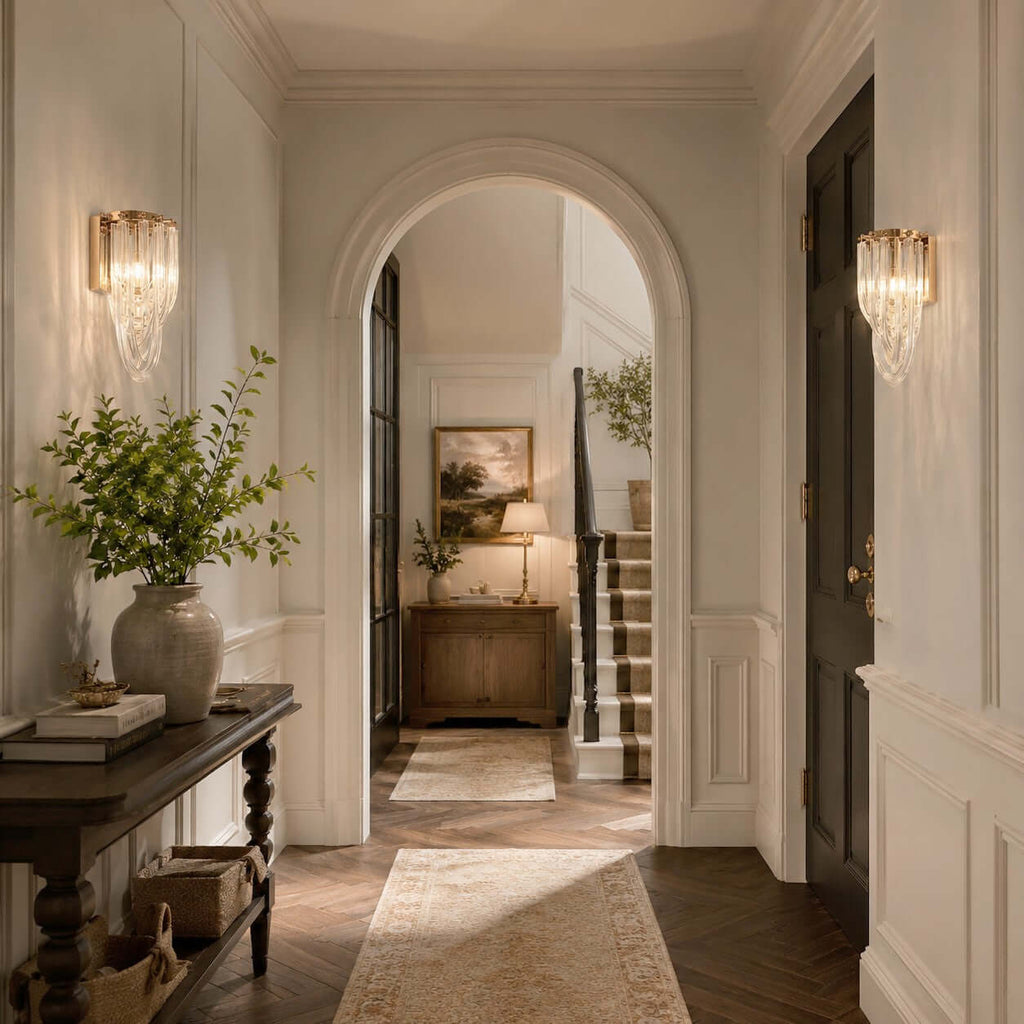 In a hallway with an arched opening and herringbone floor, a pair of Clérachic wall lights glow either side of a console.