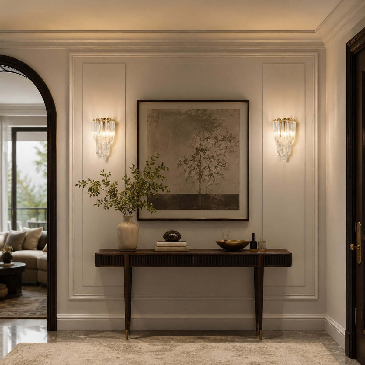 Two Clérachic wall lights frame a landscape print above a slim dark console table, in a panelled hall by an arched opening.