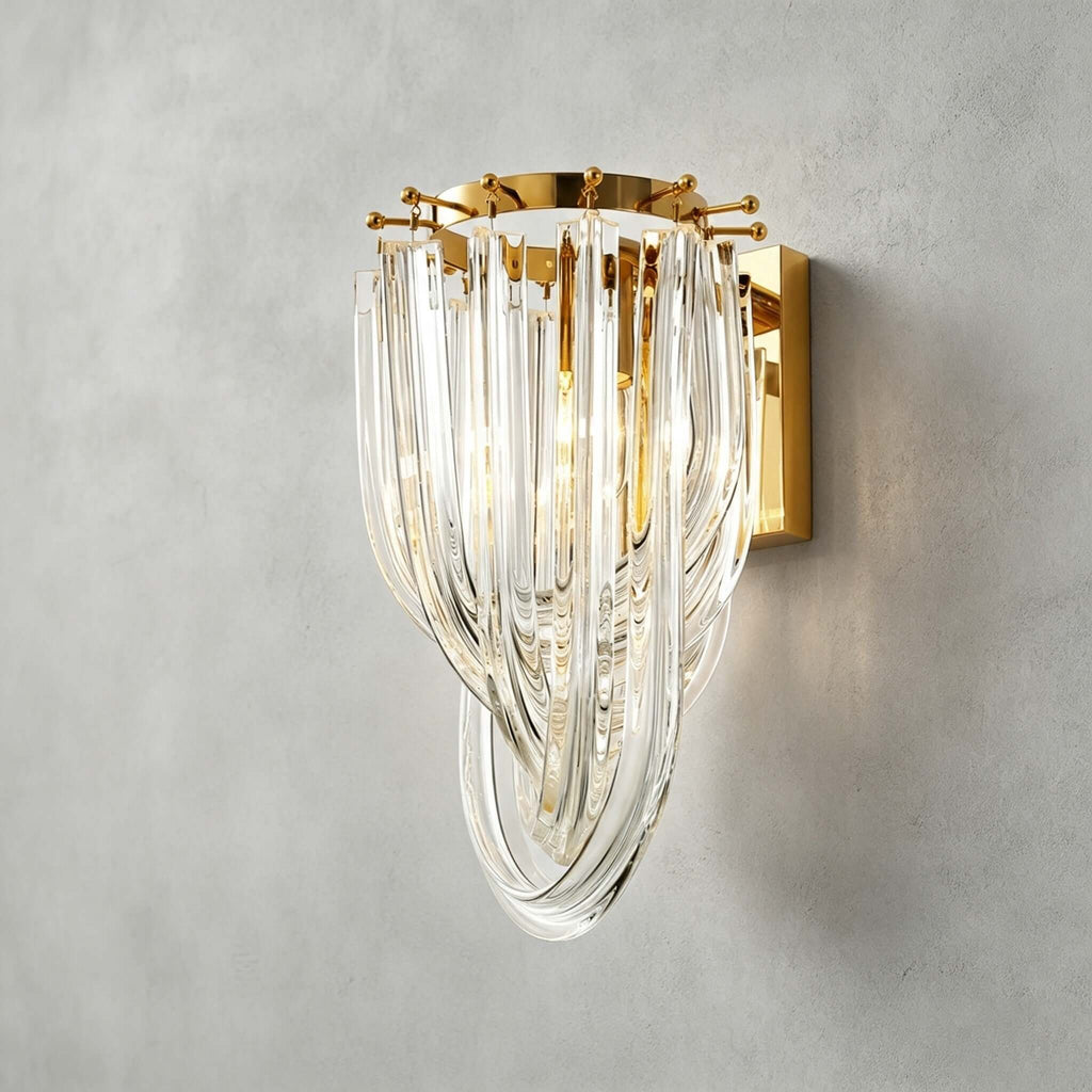 Close view of the looped clear glass strands and the gold backplate of this Clérachic wall light, on a grey plaster wall.