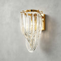 Close view of the looped clear glass strands and the gold backplate of this Clérachic wall light, on a grey plaster wall.