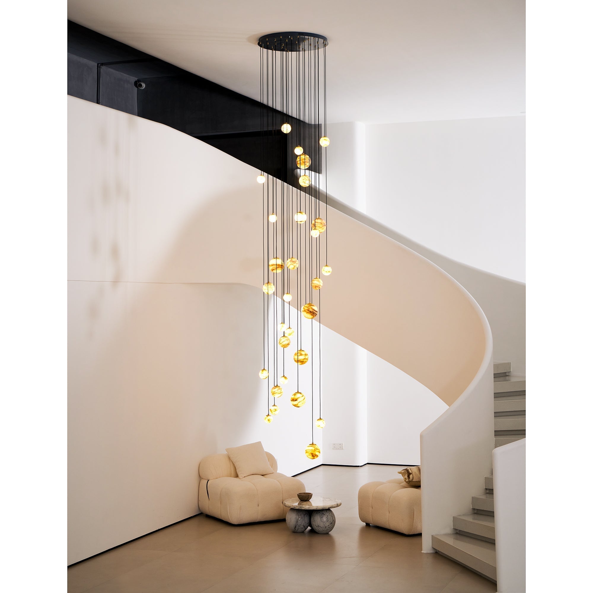 The Clérachic Cascading Globe Chandelier seen from the sofa below, its lit spheres tracing a spiral down the full height of the stairwell.