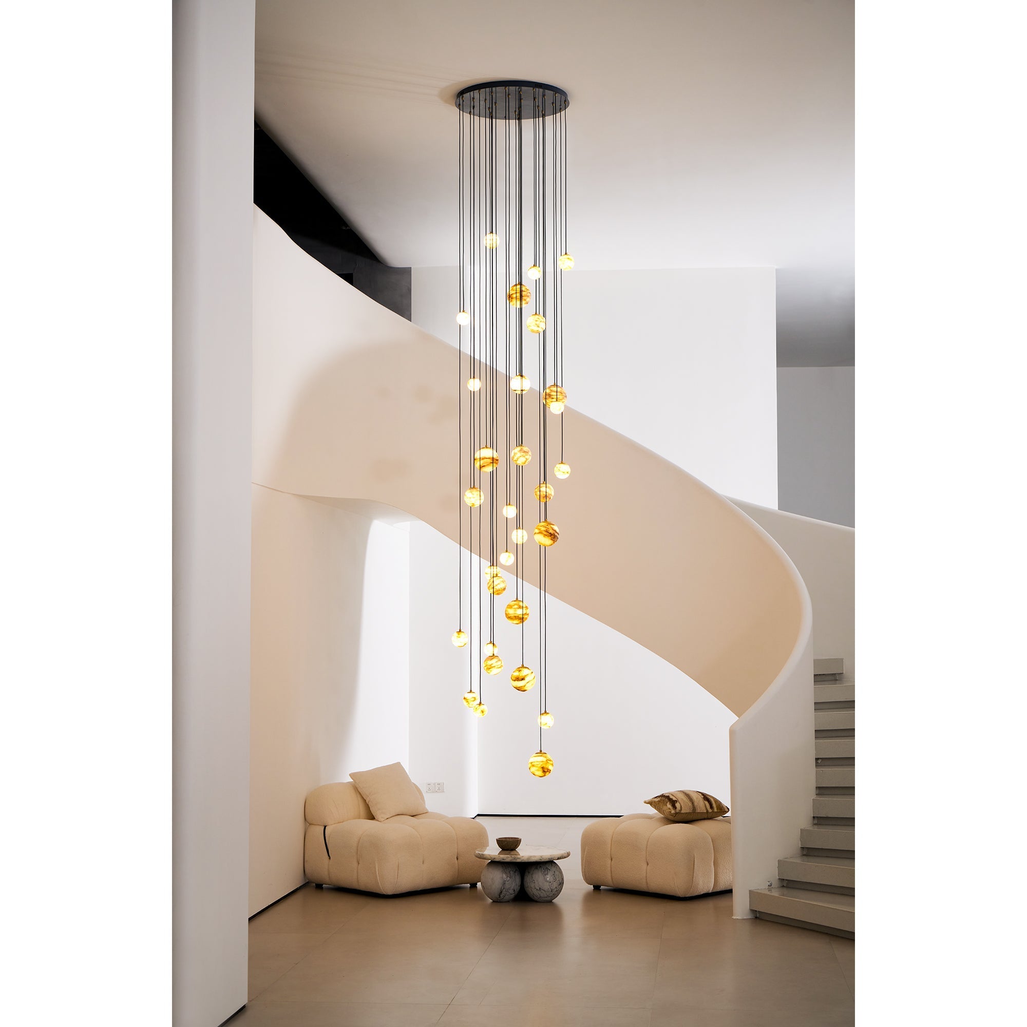 Framed by the stair curve, the Clérachic Cascading Globe Chandelier drops its glowing alabaster spheres to head height above a low table.