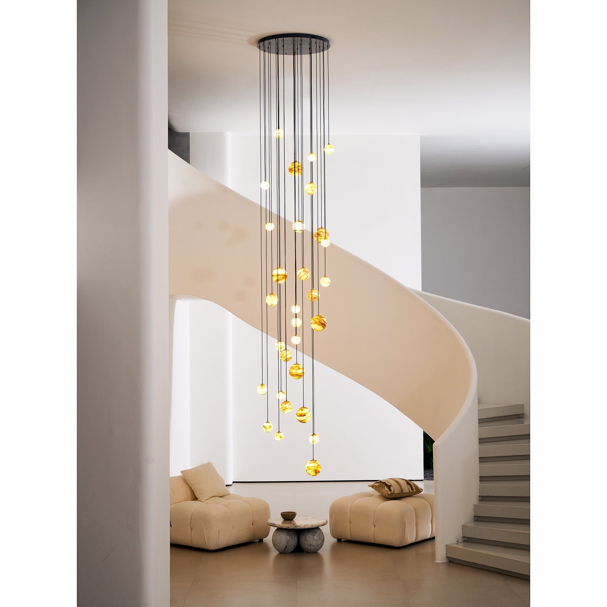The Clérachic Cascading Globe Chandelier viewed past a white pillar, the cascade of lit spheres reading as one column of warm light.