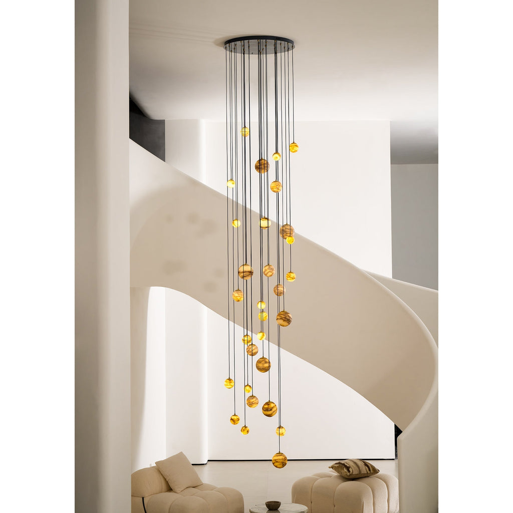 The Clérachic Cascading Globe Chandelier lit against a pale stairwell wall, staggered drops turning a group of pendants into a cascade.