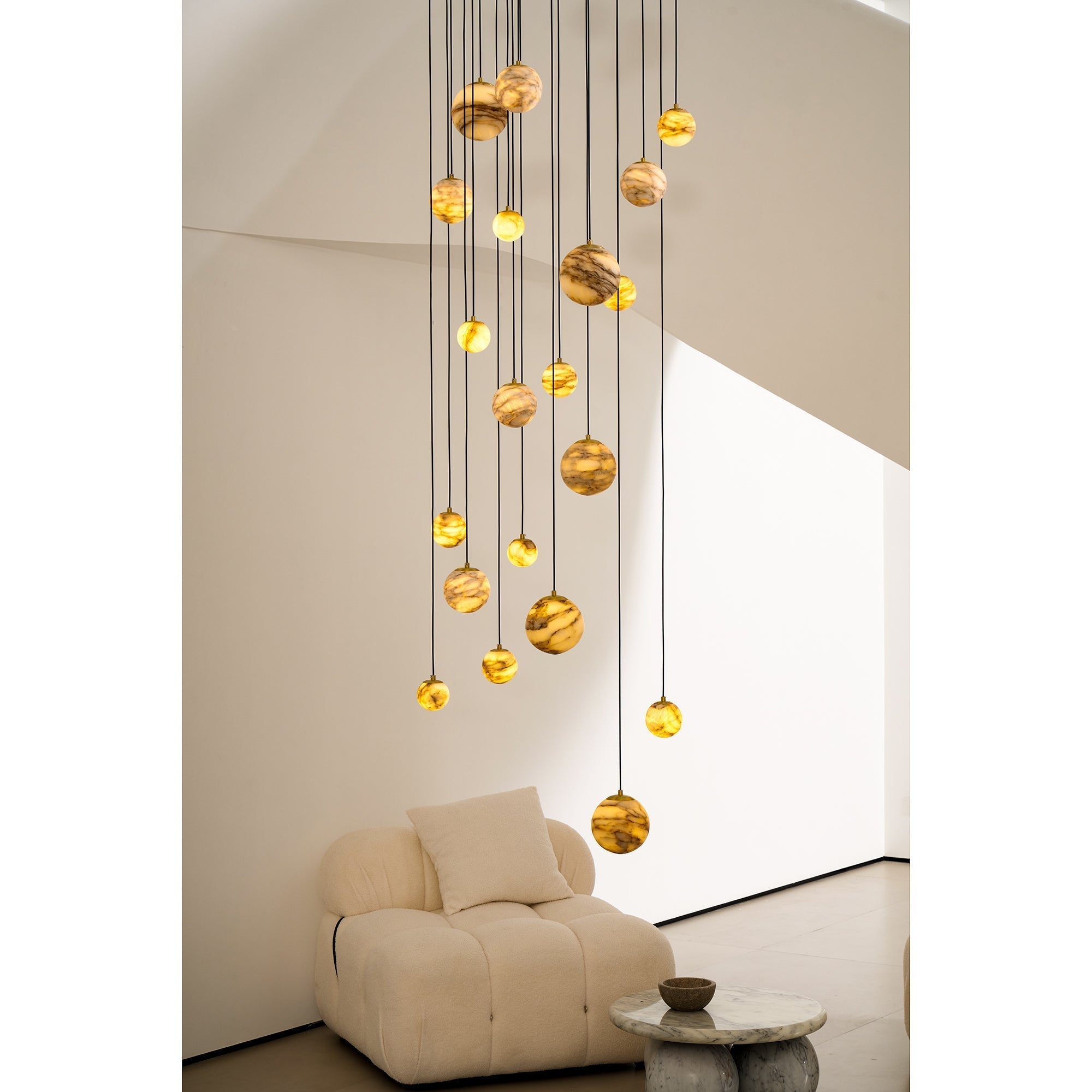 Close view of the Clérachic Cascading Globe Chandelier's lower spheres, lit alabaster showing amber banding above a bouclé armchair.