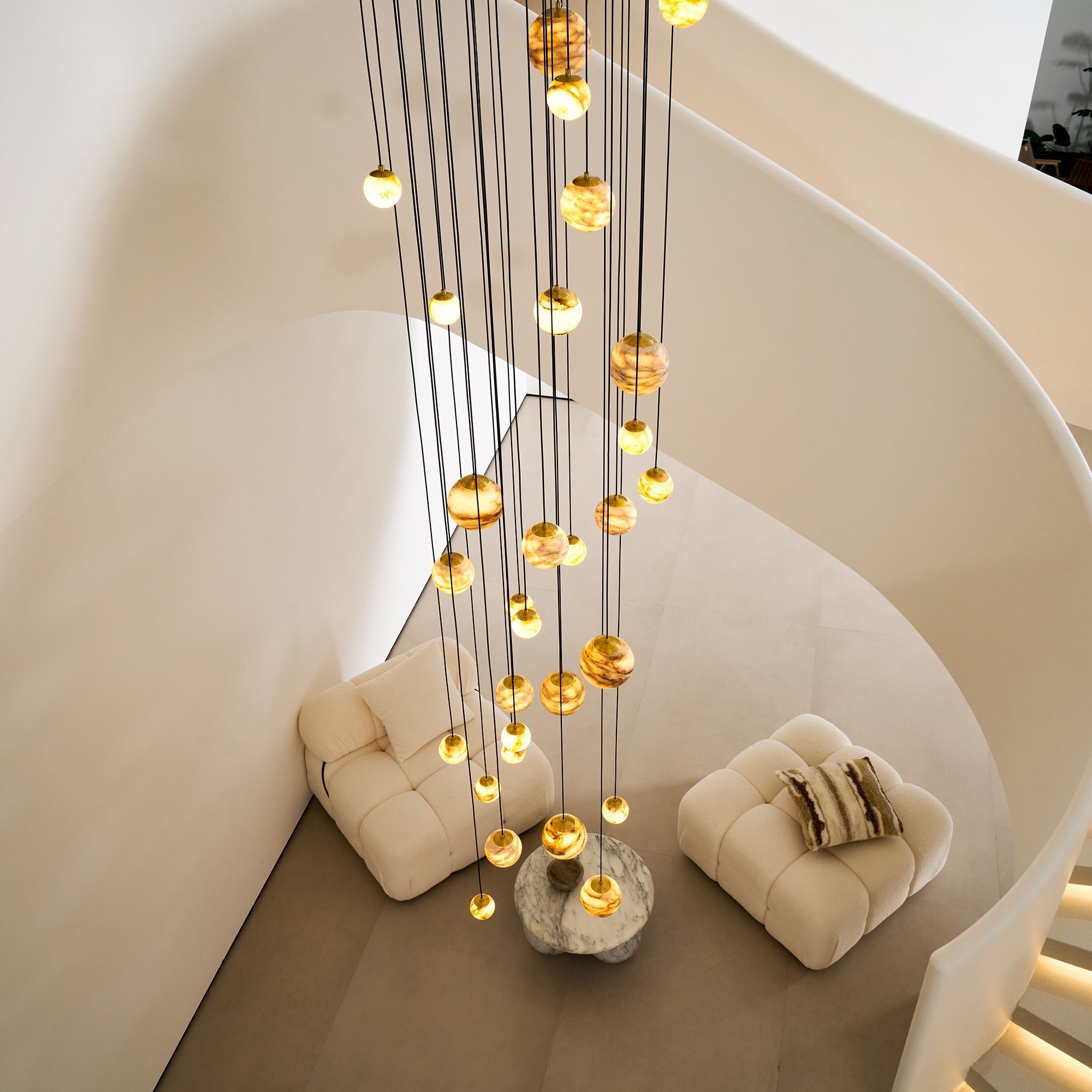 Seen from the landing above, the Clérachic Cascading Globe Chandelier's cords drop past the stair curve to the seating on the floor below.
