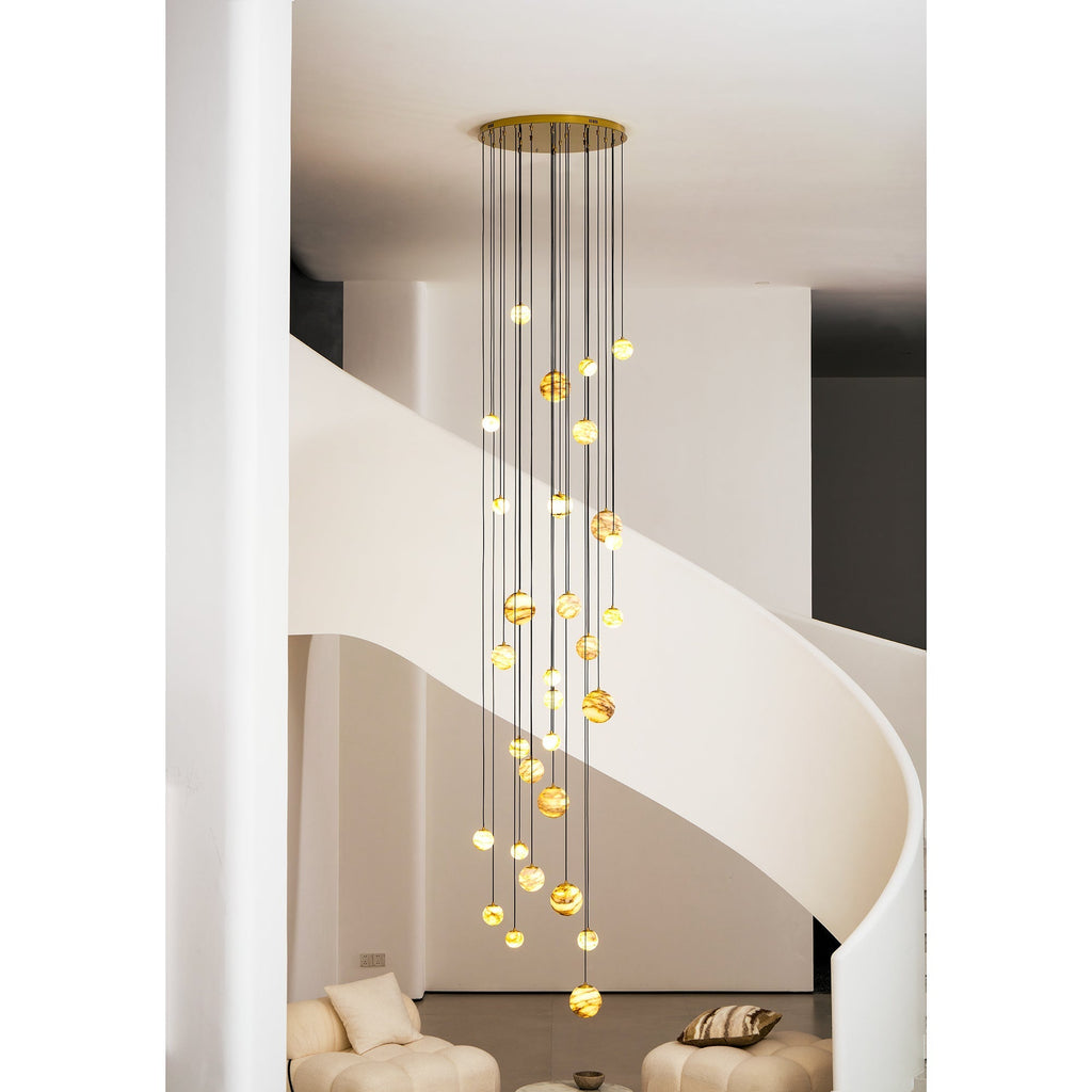 Gold-canopy version of the Clérachic Cascading Globe Chandelier lit in the stairwell, the stone deepening to honey-amber overhead.
