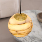 One sphere of the Clérachic Cascading Globe Chandelier photographed close, brass cap and honey-veined stone above a marble side table.
