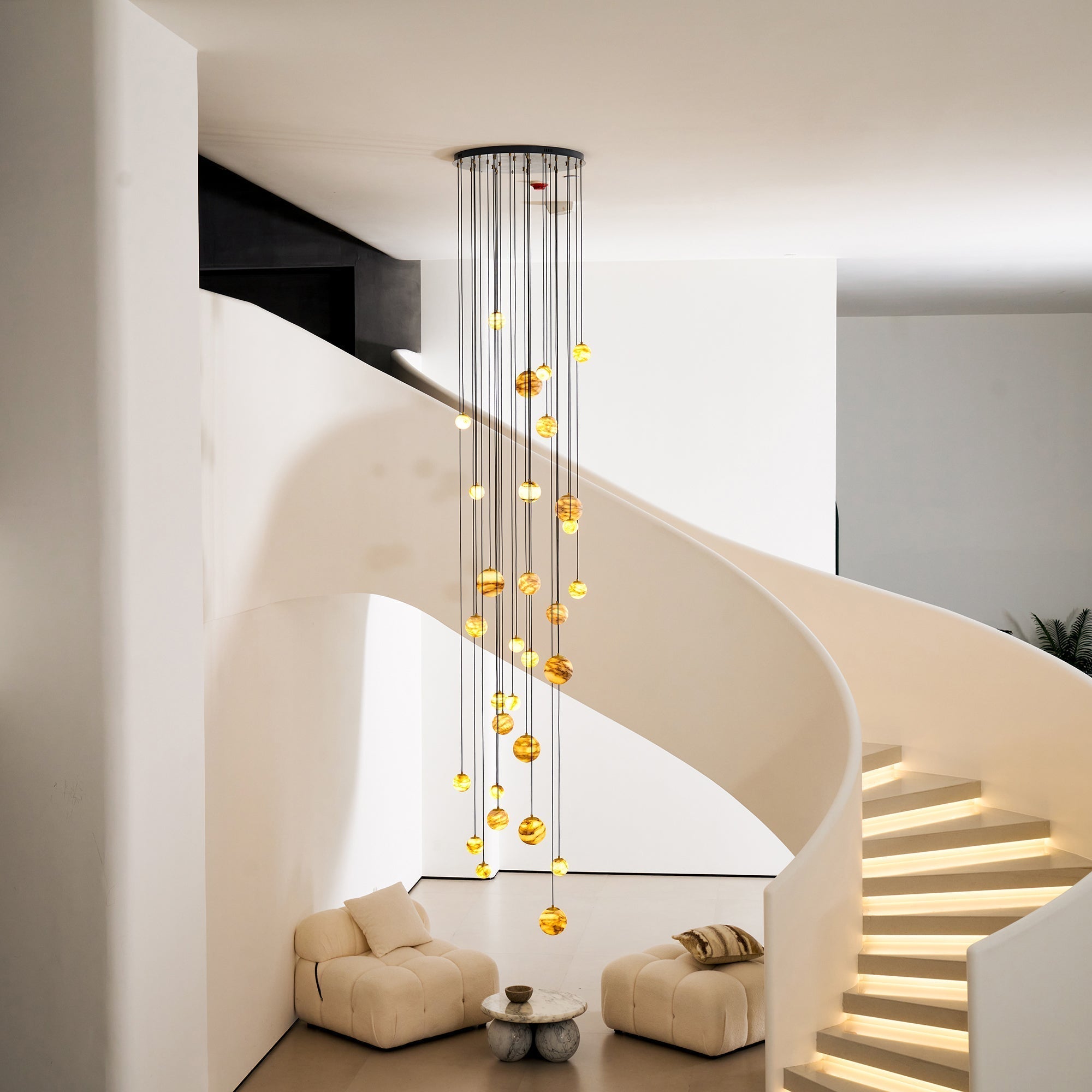 The Clérachic Cascading Globe Chandelier lit beside an illuminated spiral stair, spheres dropping to head height above the bottom step.