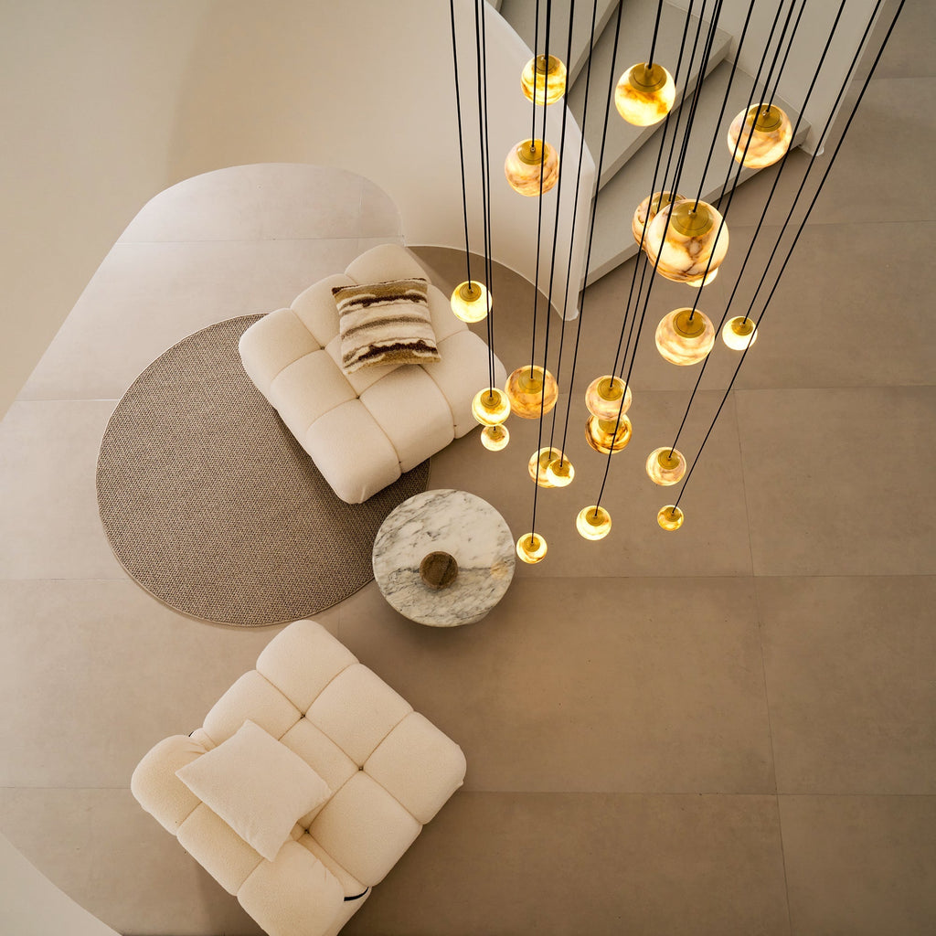 Overhead view of the Clérachic Cascading Globe Chandelier, its lit spheres scattered above two bouclé chairs and a marble coffee table.