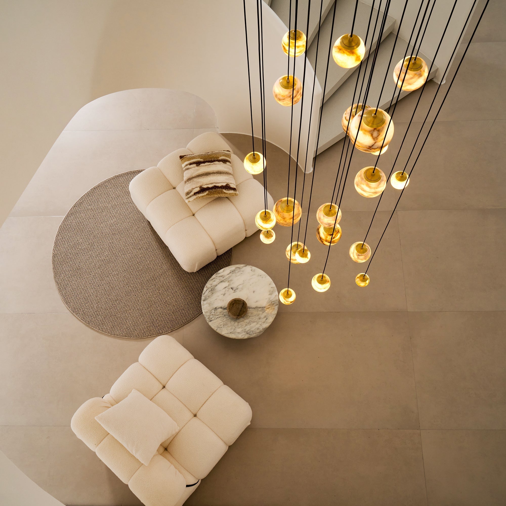 Overhead view of the Clérachic Cascading Globe Chandelier, its lit spheres scattered above two bouclé chairs and a marble coffee table.