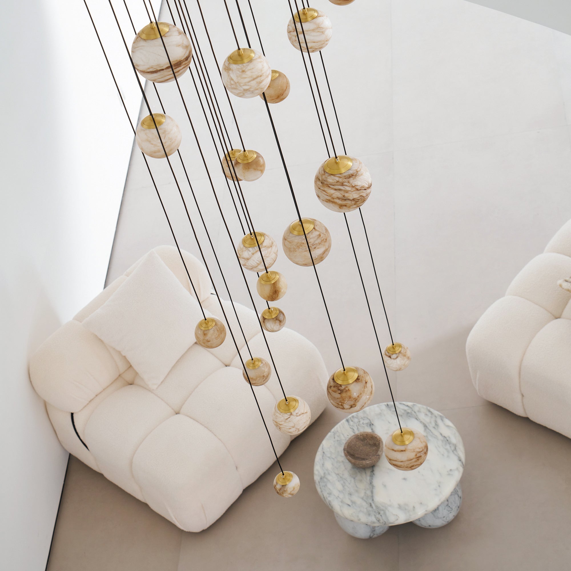 Unlit by day, the Clérachic Cascading Globe Chandelier spheres read warm off-white, banding shifting from one quarried stone to the next.