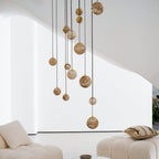 The lower half of the Clérachic Cascading Globe Chandelier against a white wall, mixed sphere sizes staggered above a bouclé seat.