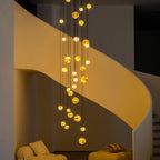 The Clérachic Cascading Globe Chandelier after dark, lit spheres washing the curved stair wall in amber against a darkened room.