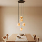 The Clérachic cascading globe chandelier in its five-head configuration above an oak dining table, each alabaster sphere hung on its own flex at its own height