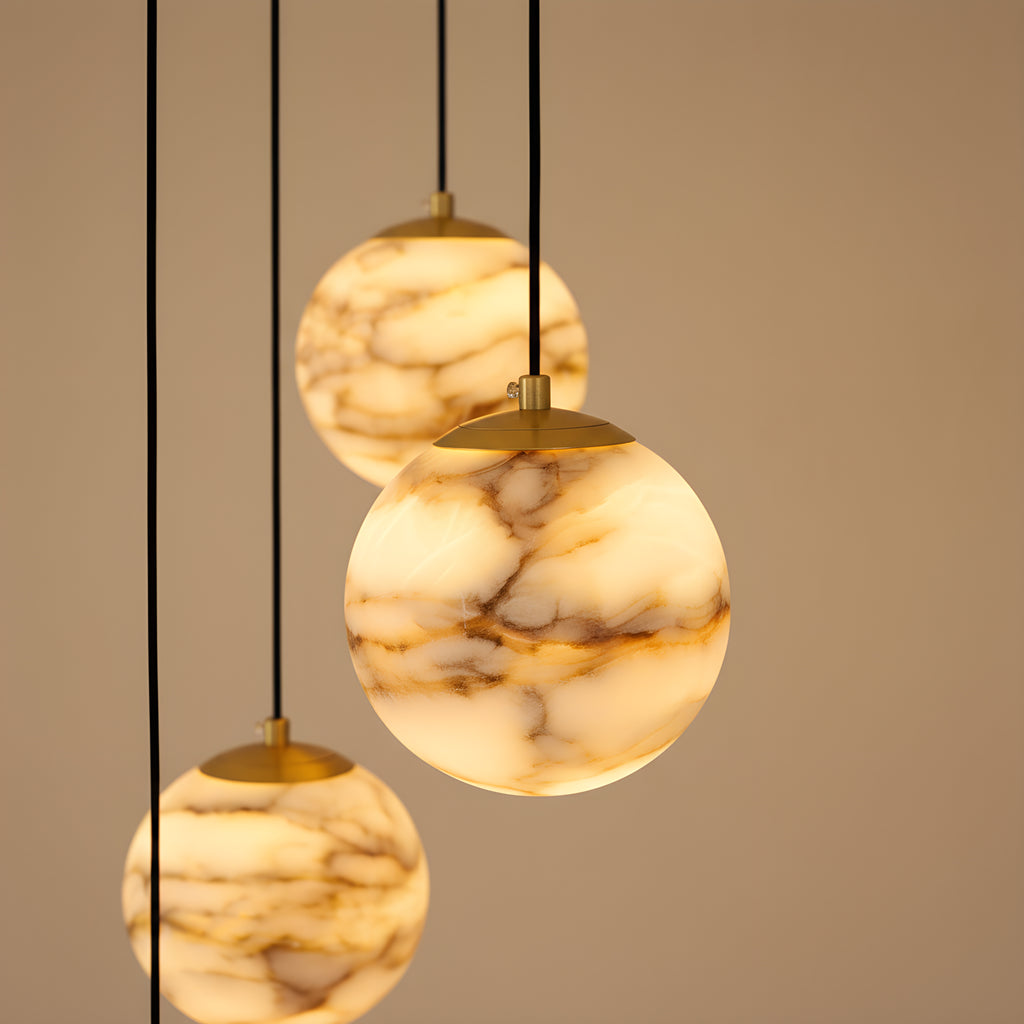 Close view of three lit alabaster spheres with their brushed brass caps, the tan and caramel banding reading as strata through the stone