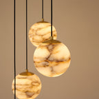 Close view of three lit alabaster spheres with their brushed brass caps, the tan and caramel banding reading as strata through the stone