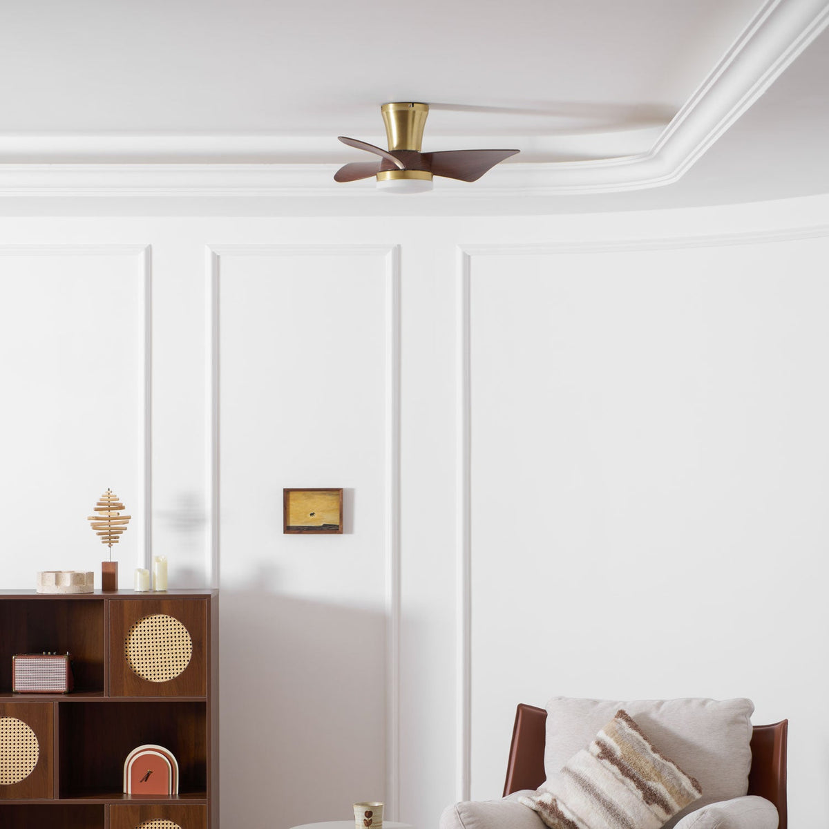 A small Clérachic ceiling fan in gold and walnut sits high on a white ceiling, above panelled walls and a wooden cabinet with cane doors.