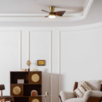 The Clérachic gold and walnut ceiling fan close to the ceiling, above a panelled wall, a cane-fronted shelf and a leather-and-linen armchair.