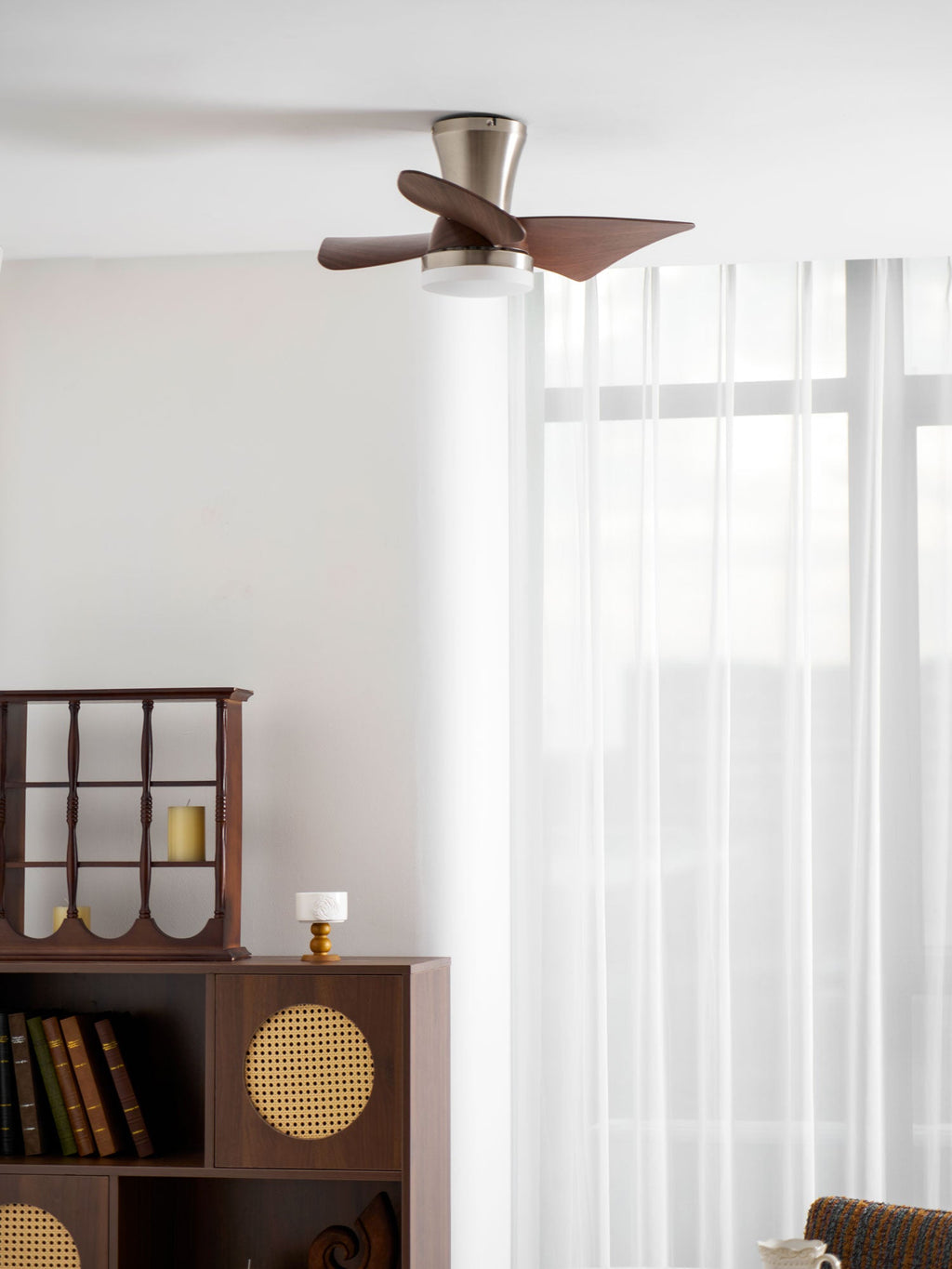 Looking up at the Clérachic nickel ceiling fan, with a lit globe light, over a bookshelf, a cane cabinet and a round table with a cloth.