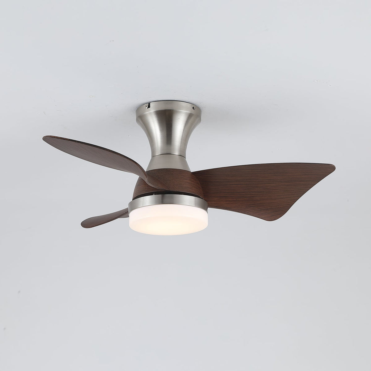 The Clérachic nickel fan with its light on a warm setting, three walnut-grain blades spread out against a pale grey ceiling.
