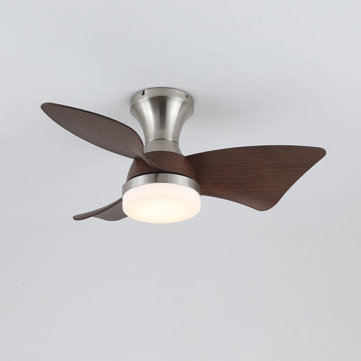 A Clérachic ceiling fan in nickel with walnut-grain blades and a warm light, seen at a slight angle from below on grey.